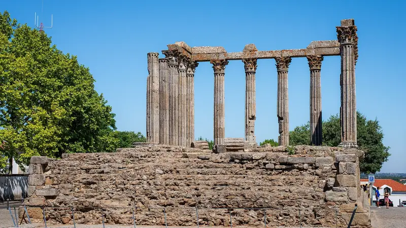 The granite columns of Évora's Roman temple standing on their stone base under a blue sky.