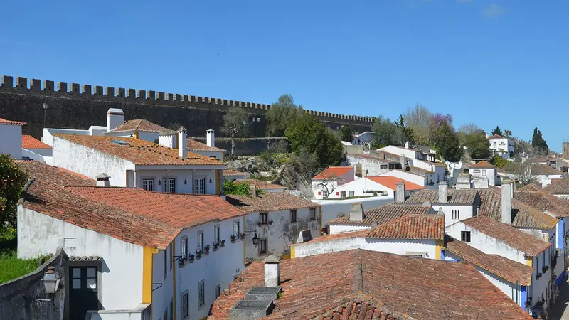 White houses with red-tiled roofs inside Óbidos, with the battlements of the town wall behind them.