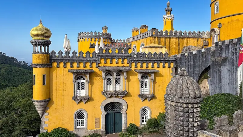 The yellow walls, battlements and domed turret of Pena Palace in Sintra under a blue sky.