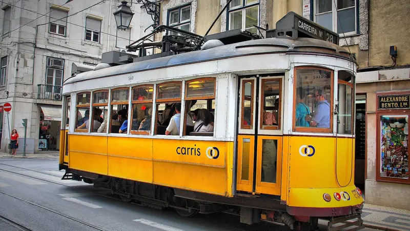 A yellow Carris tram full of passengers in a narrow Lisbon street.